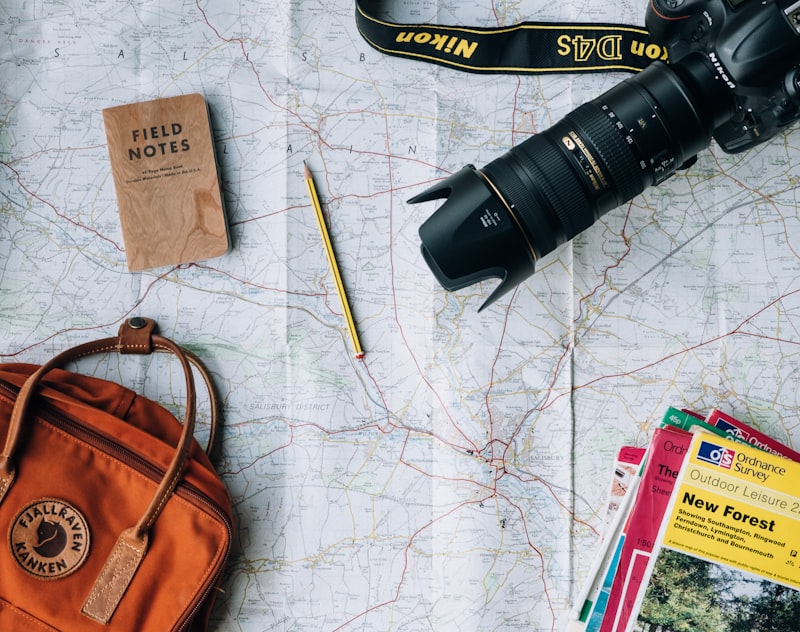Travel gear flatlay with backpack, camera, sunglasses, and map